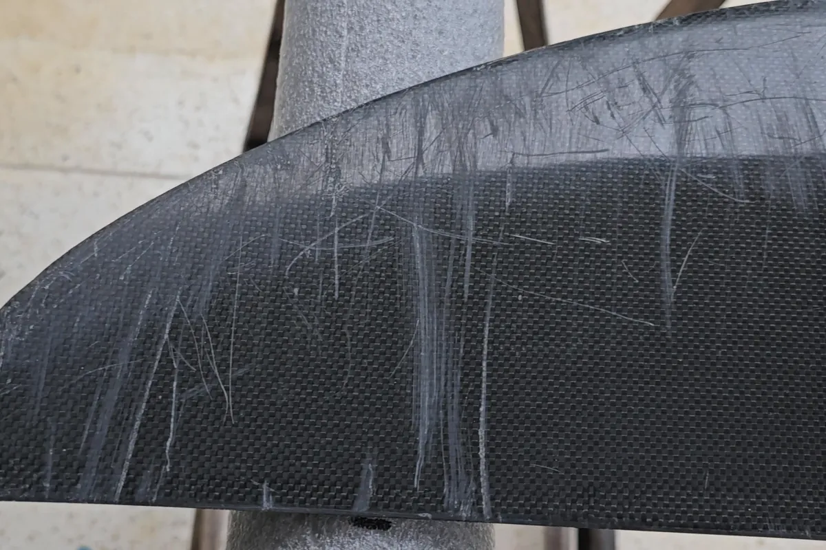Carbon front wing covered in deep white scratches around the mounting holes